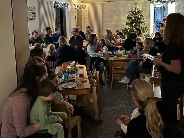 Eltern und Kinder sitzen an gedeckten Tischen, im Hintergrund ein geschmückter Weihnachtsbaum