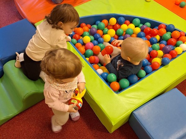 1 Kind sitzt im Bällebad, 2 weitere Kinder spielen mit