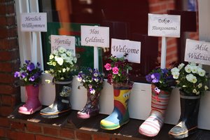 Bunte Gummistiefel mit Blumen bepflanzt und Willkommensschildern in verschiedenen Sprachen, Foto: Pixabay