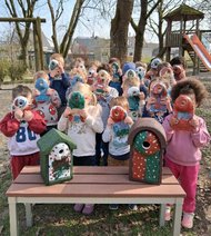 Kinder zeigen bunt bemalte Vogelhäuser vor ihren Gesichtern