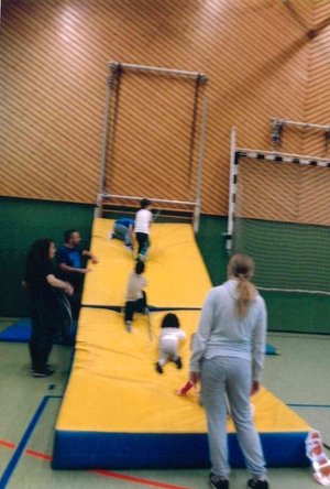 Kinder krabbeln unter Beaufsichtigung einer Betreuung an einer Mattenwand hoch