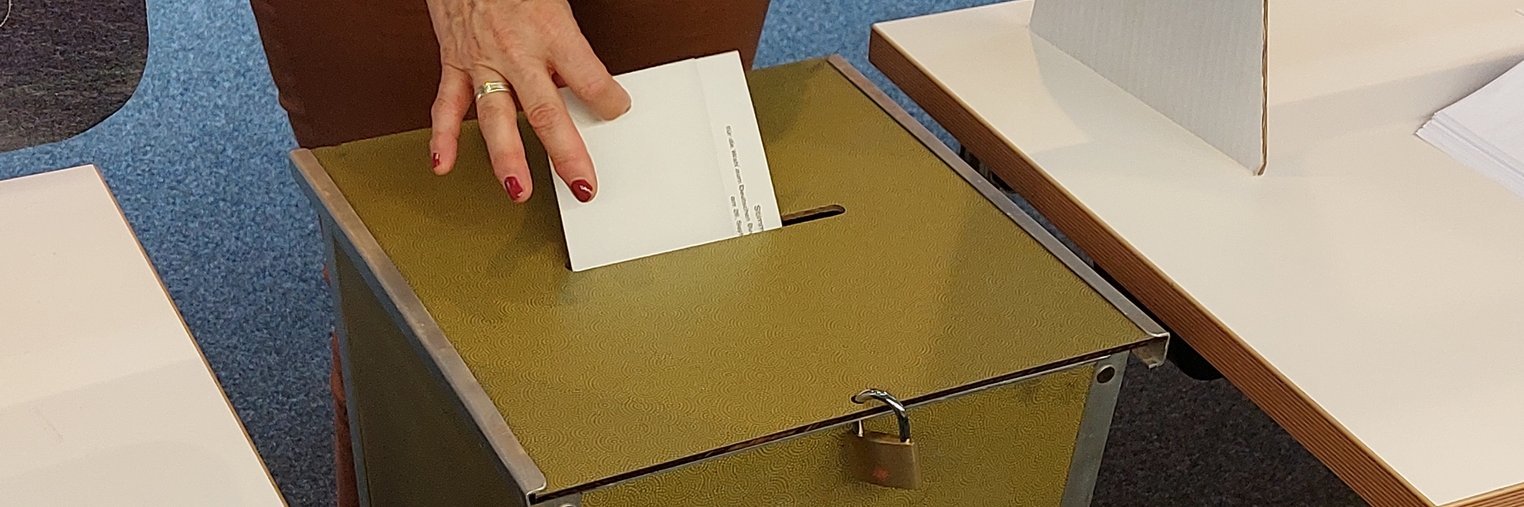 Ein Stimmzettelumschlag wird in eine Wahlurne eingeworfen