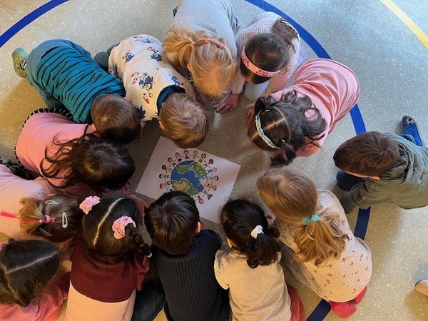 Blick von oben auf eine Runde Kinder, die über einem Bild der Erdkugel hocken