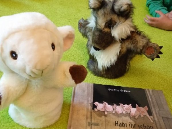 Handpuppen Wolf und Schaf neben Bilderbuch "Habt ihr schon vom Wolf gehört?"