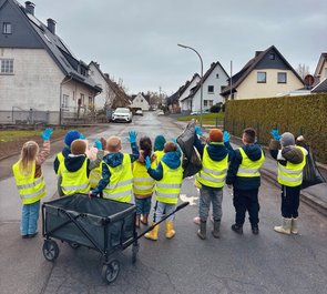 Kindergartengruppe mit Warnwesten, Bollerwagen und blauen Handschuhen auf dem Weg durch Suttrop