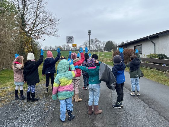 Kindergartengruppe auf einem Weg, die Kinder heben die Hände und zeigen blaue Handschuhe