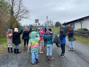 Kindergartengruppe auf einem Weg, die Kinder heben die Hände und zeigen blaue Handschuhe
