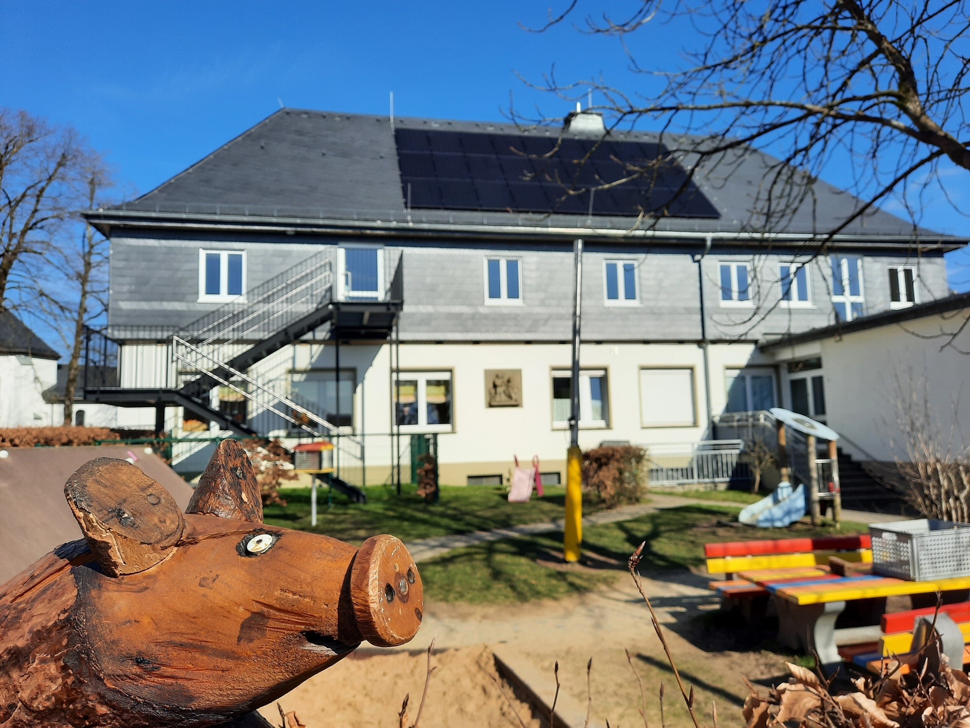 Blick auf das KiTa-Gebäude, im Vordergrund sieht man den Spielplatz